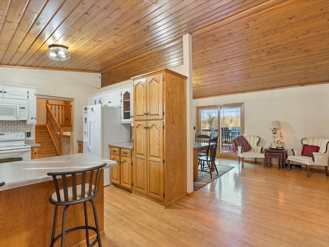 kitchen with lofted ceiling, white appliances, a kitchen breakfast bar, light countertops, and light wood-type flooring