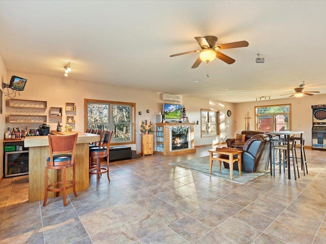 interior space featuring a dry bar, a warm lit fireplace, baseboards, ceiling fan, and wine cooler