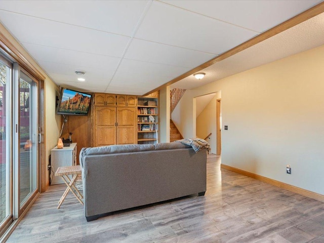 living area with a drop ceiling, stairway, light wood-type flooring, and baseboards