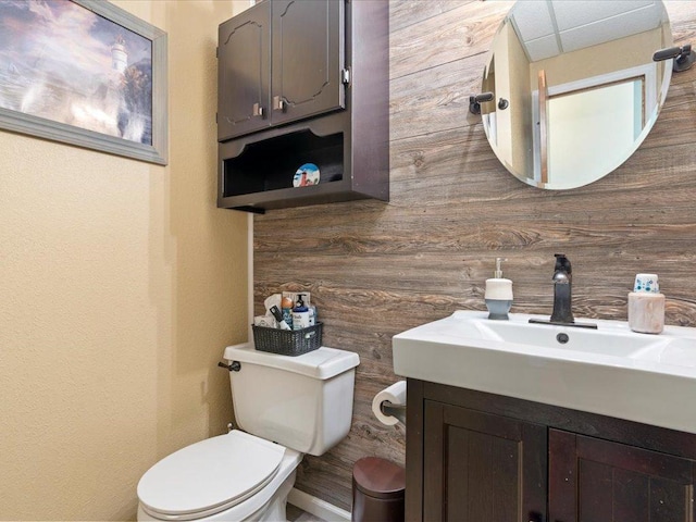 bathroom featuring toilet, wood walls, and vanity