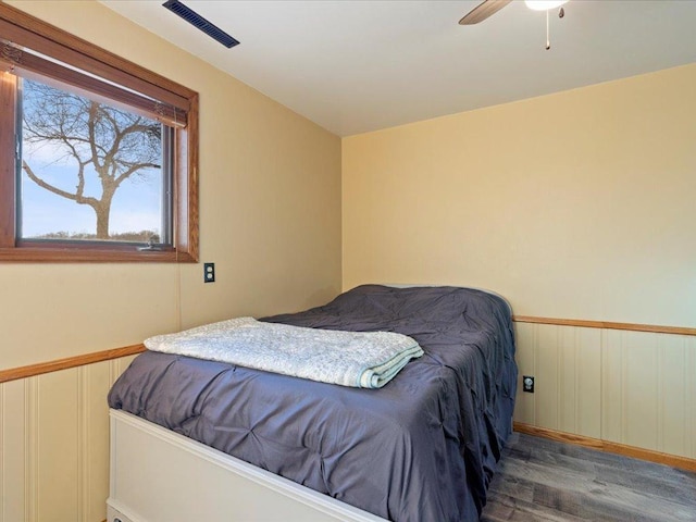 bedroom with a ceiling fan, wainscoting, visible vents, and wood finished floors