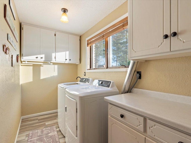 clothes washing area with a textured ceiling, a textured wall, baseboards, washer and dryer, and cabinet space