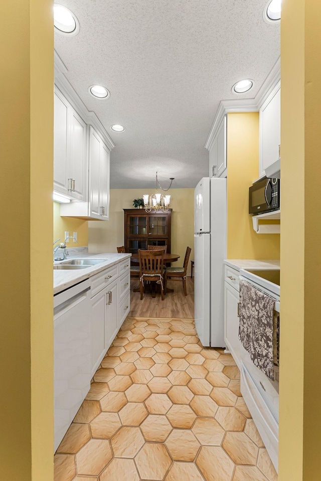 kitchen featuring white appliances, white cabinetry, light countertops, and a sink