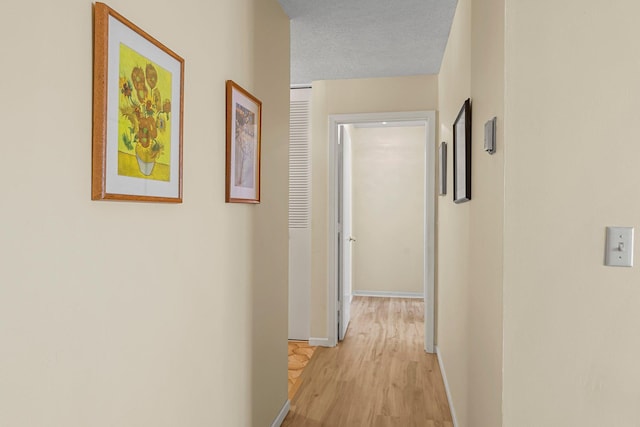 hall with a textured ceiling, light wood-type flooring, and baseboards