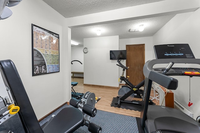 exercise room with baseboards, a textured ceiling, and wood finished floors