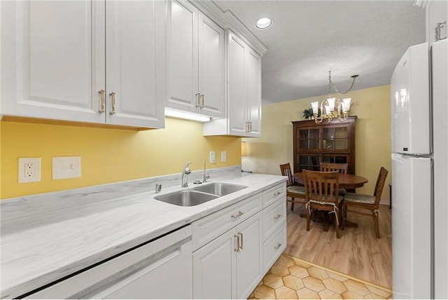 kitchen featuring white appliances, a sink, light countertops, white cabinetry, and a notable chandelier