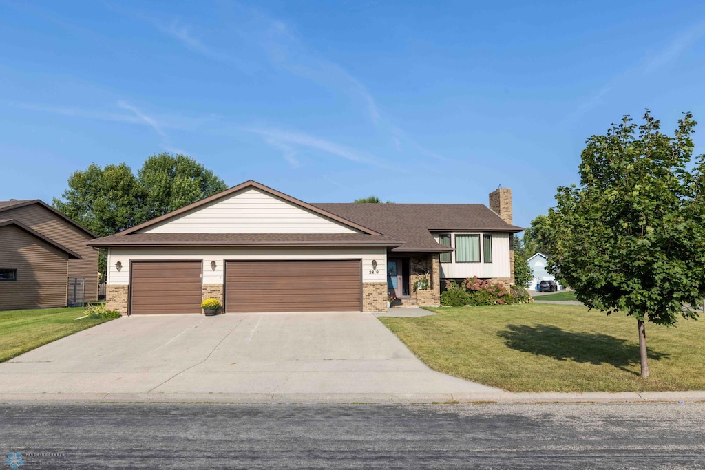 view of front of property with brick siding, a chimney, concrete driveway, a garage, and a front lawn