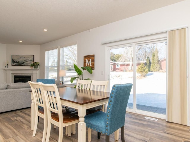 dining area with a glass covered fireplace, a healthy amount of sunlight, visible vents, and wood finished floors