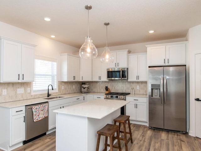 kitchen with wood finished floors, a sink, white cabinets, appliances with stainless steel finishes, and a center island