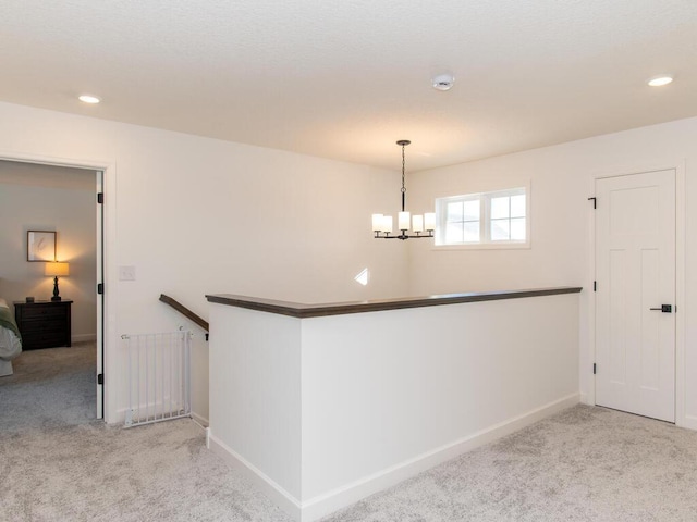 hall featuring carpet, baseboards, a notable chandelier, and an upstairs landing