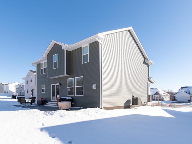 snow covered rear of property featuring entry steps, a residential view, and cooling unit