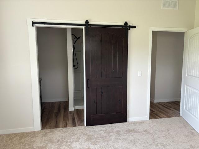 unfurnished bedroom featuring baseboards, a barn door, visible vents, and carpet flooring