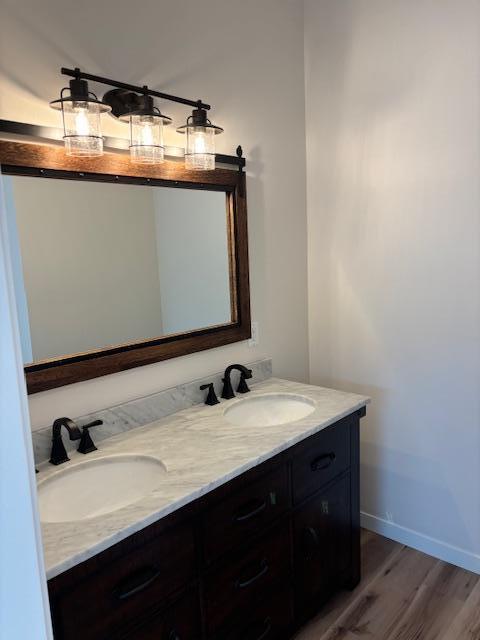 bathroom featuring double vanity, baseboards, a sink, and wood finished floors