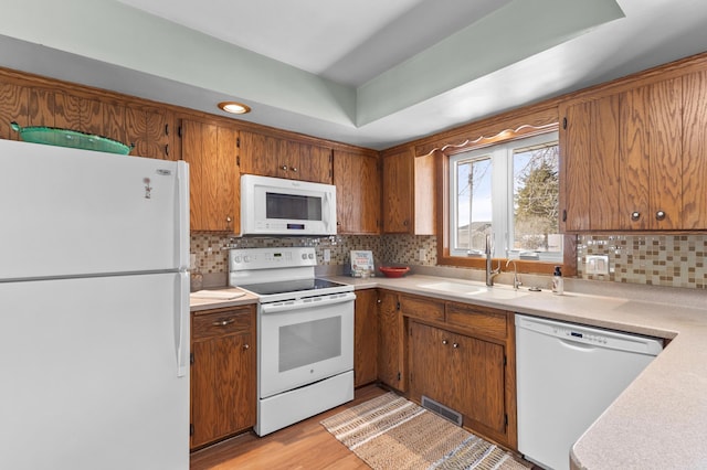 kitchen with light wood-style flooring, white appliances, a sink, light countertops, and brown cabinetry