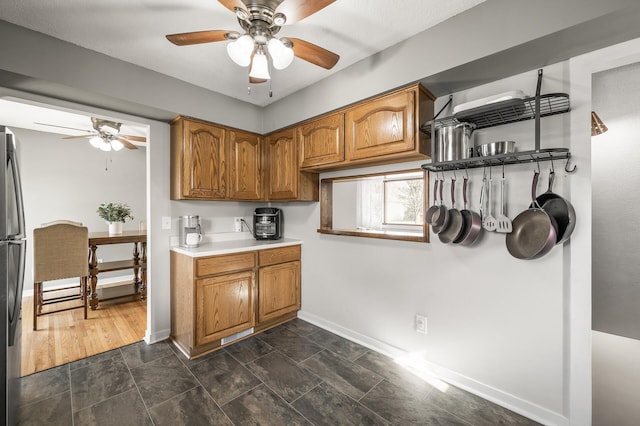 kitchen with a ceiling fan, light countertops, baseboards, and brown cabinets