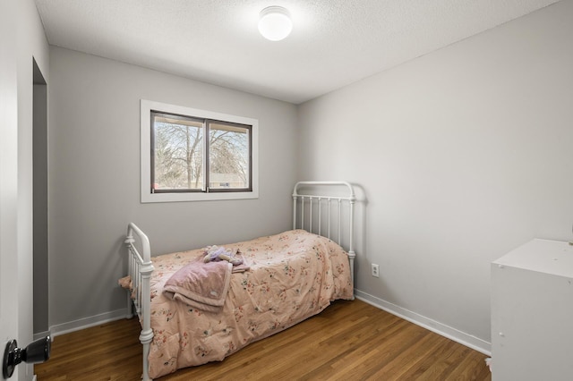 bedroom featuring a textured ceiling, baseboards, and wood finished floors