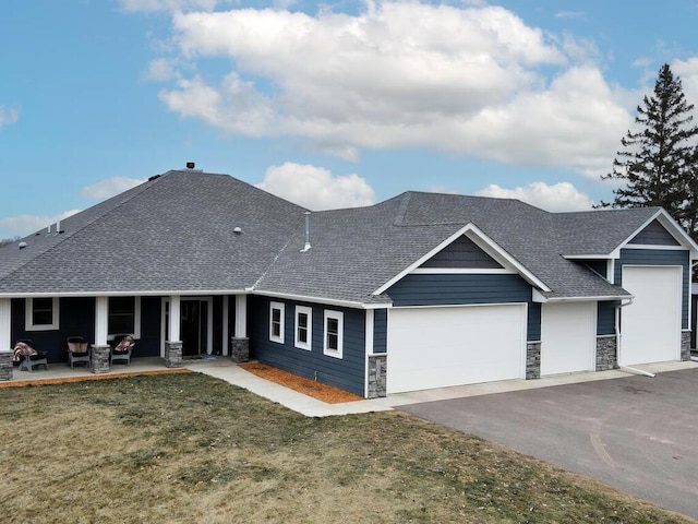 view of front facade featuring a garage, driveway, stone siding, roof with shingles, and a front yard