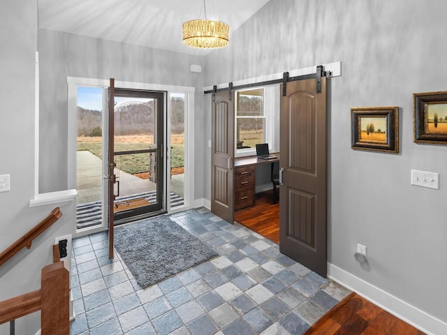 foyer entrance featuring a barn door, a notable chandelier, a towering ceiling, baseboards, and stone tile flooring