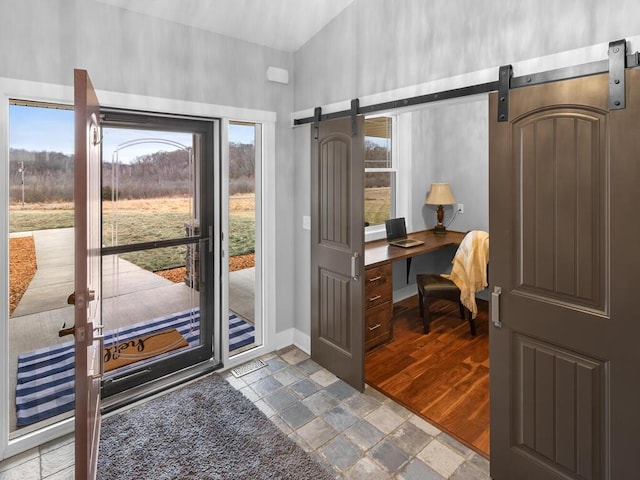 doorway with a barn door, stone tile flooring, and baseboards