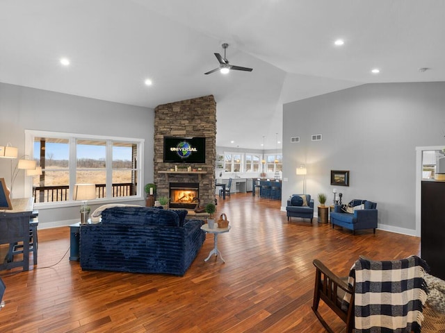 living area with high vaulted ceiling, visible vents, a stone fireplace, and wood finished floors