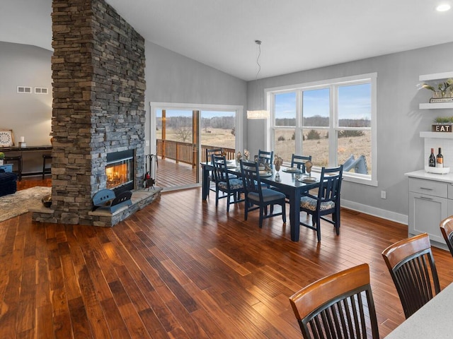 dining space with dark wood-style floors, a stone fireplace, vaulted ceiling, and baseboards