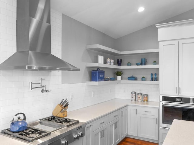 kitchen featuring lofted ceiling, wall chimney range hood, stainless steel appliances, and light countertops