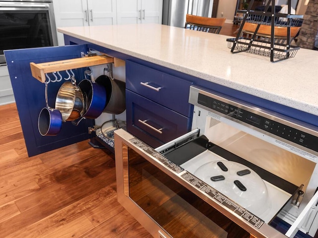 room details featuring light wood-type flooring, light stone countertops, oven, and blue cabinets