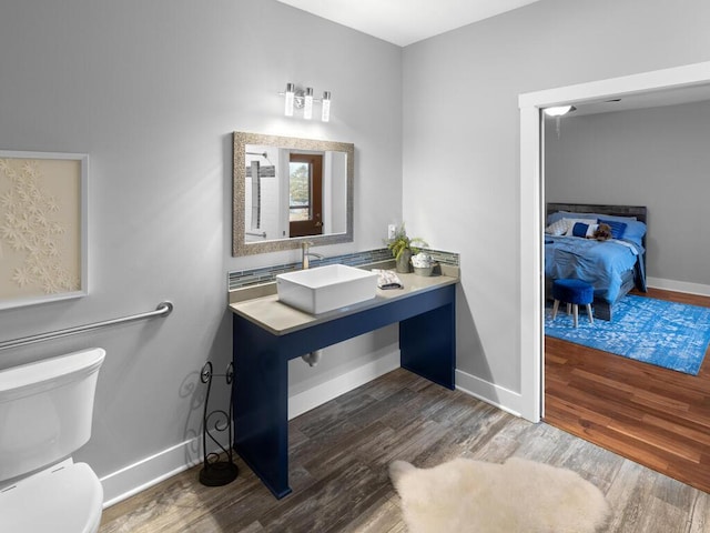 ensuite bathroom with baseboards, a sink, toilet, and wood finished floors