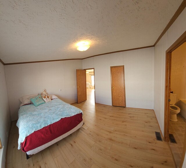 bedroom featuring light wood-type flooring, visible vents, crown molding, and a textured ceiling