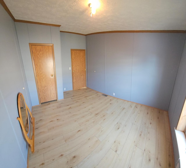 unfurnished bedroom with a textured ceiling, light wood finished floors, visible vents, and crown molding