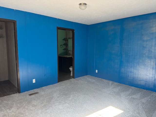 empty room with a textured ceiling, carpet flooring, a sink, and visible vents