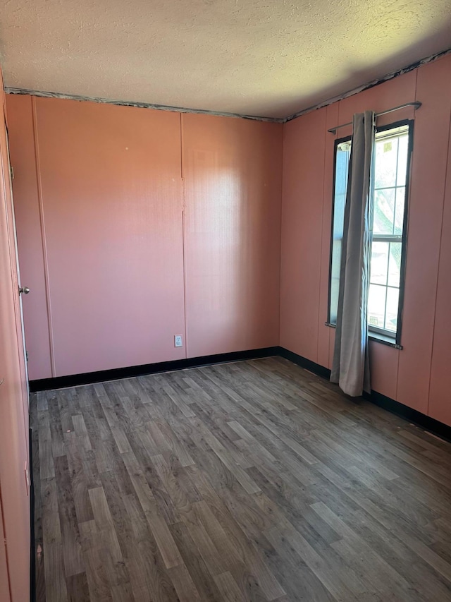 unfurnished room featuring a textured ceiling, wood finished floors, and baseboards