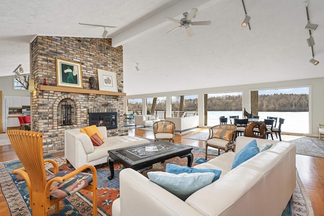 living room with a fireplace, rail lighting, a textured ceiling, wood finished floors, and high vaulted ceiling