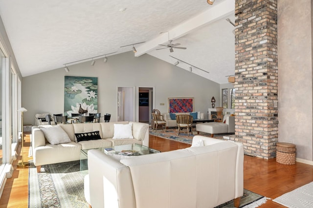 living area featuring vaulted ceiling with beams, rail lighting, light wood-style flooring, and a ceiling fan