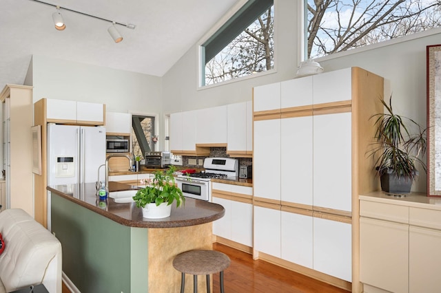 kitchen featuring high vaulted ceiling, a breakfast bar area, white appliances, a sink, and light wood-style floors