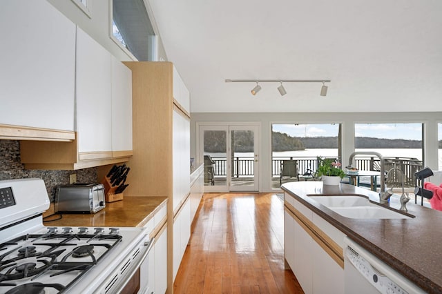 kitchen featuring dark countertops, light wood-style flooring, white cabinetry, a sink, and white appliances