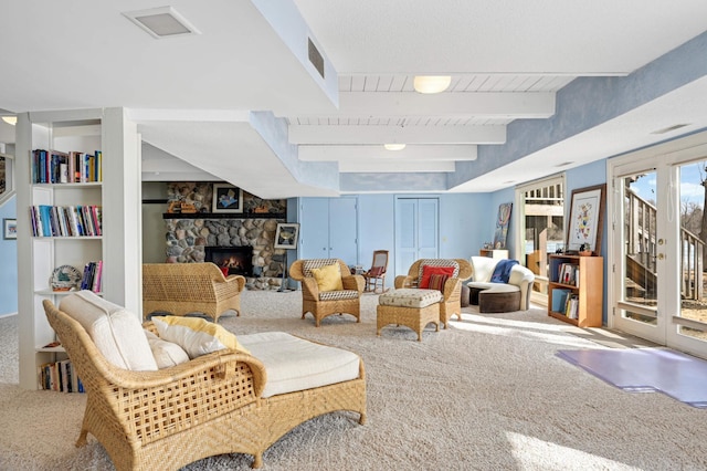 sitting room featuring carpet, visible vents, beam ceiling, and a stone fireplace