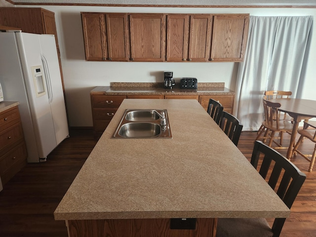 kitchen with white refrigerator with ice dispenser, dark wood-style flooring, a breakfast bar, a sink, and an island with sink