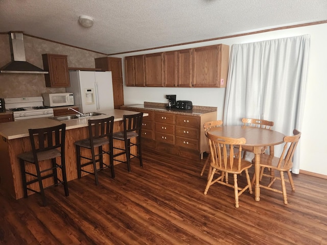 kitchen with white appliances, dark wood-style floors, vaulted ceiling, wall chimney range hood, and a sink