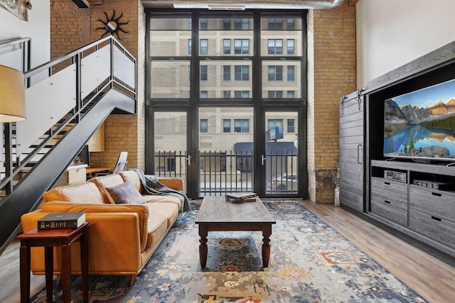 living room with a wealth of natural light, stairway, wood finished floors, and a towering ceiling