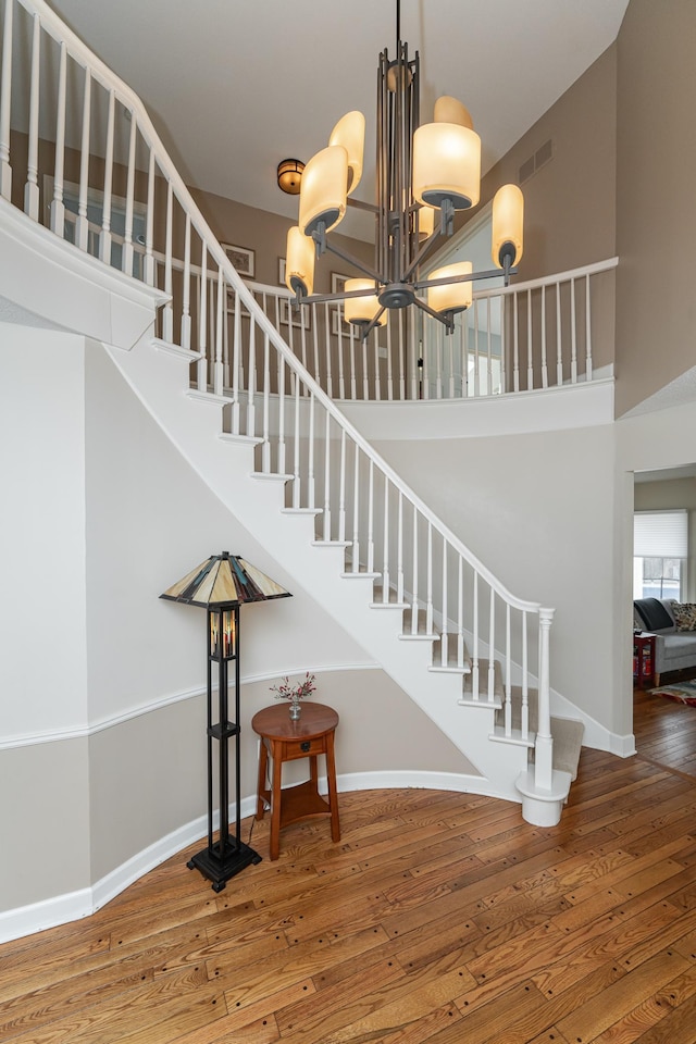 stairway featuring baseboards, visible vents, a towering ceiling, hardwood / wood-style flooring, and an inviting chandelier