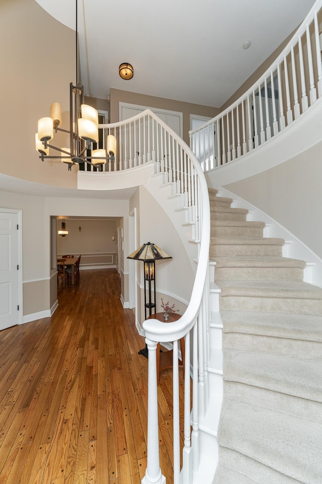 stairway featuring a towering ceiling, hardwood / wood-style flooring, baseboards, and a chandelier