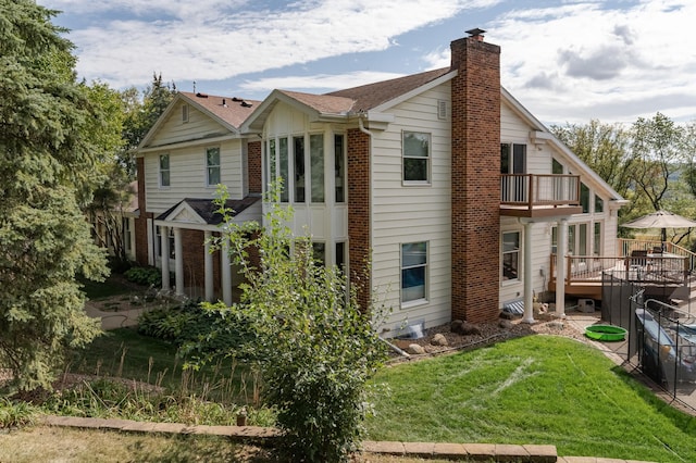 view of side of home featuring a balcony, brick siding, a chimney, and a yard