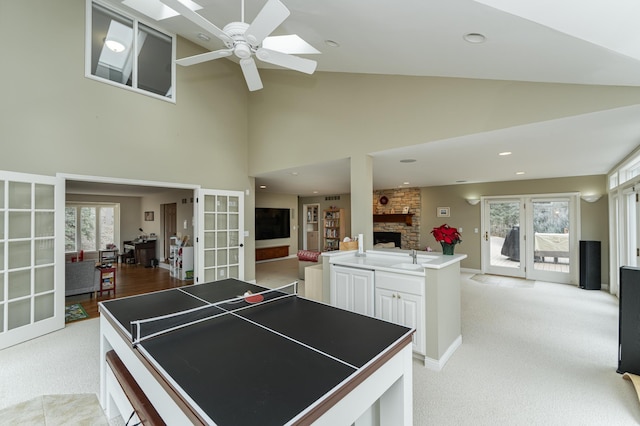 recreation room featuring plenty of natural light, a ceiling fan, a stone fireplace, and french doors