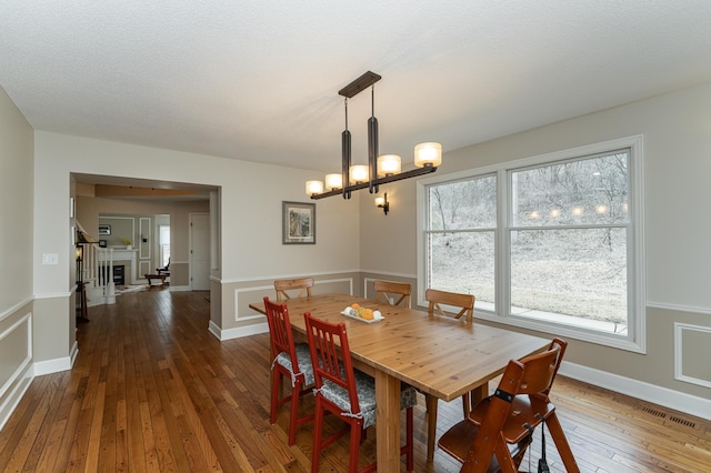 dining space with visible vents, wainscoting, wood-type flooring, a fireplace, and a notable chandelier