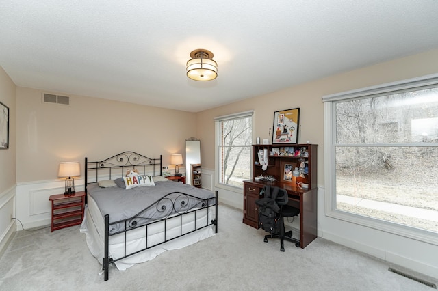 bedroom with carpet floors, visible vents, a textured ceiling, and wainscoting