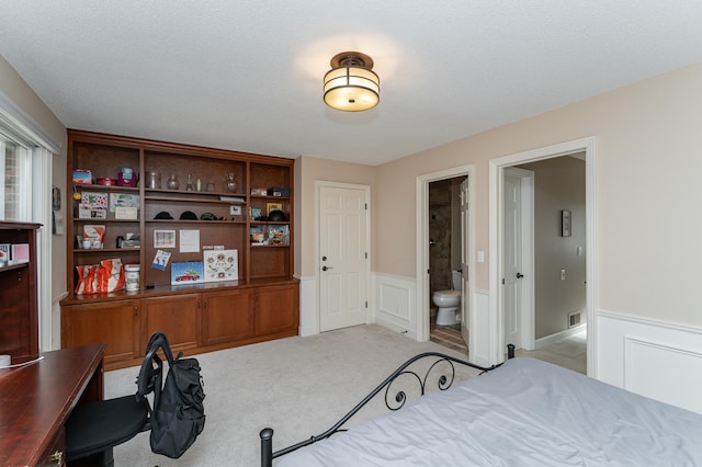 bedroom with light carpet, a wainscoted wall, visible vents, and ensuite bathroom