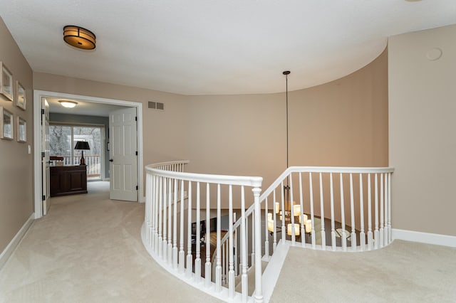 hallway featuring baseboards, carpet flooring, visible vents, and an upstairs landing