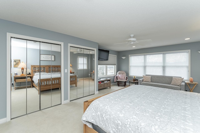 bedroom with multiple closets, a ceiling fan, light carpet, a textured ceiling, and baseboards