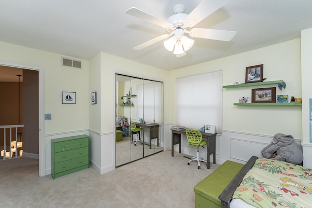 carpeted bedroom with a closet, visible vents, ceiling fan, and wainscoting